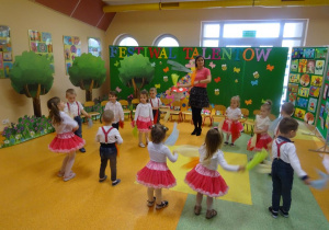Dzieci tańczą w kole, w rękach trzymają chusteczki, które unoszą przed sobą z boku do boku.